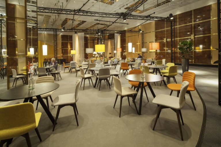 Lounge with grey, orange and yellow upholstered chairs and dark round tables at ISM Pro Sweets 2017, Cologne