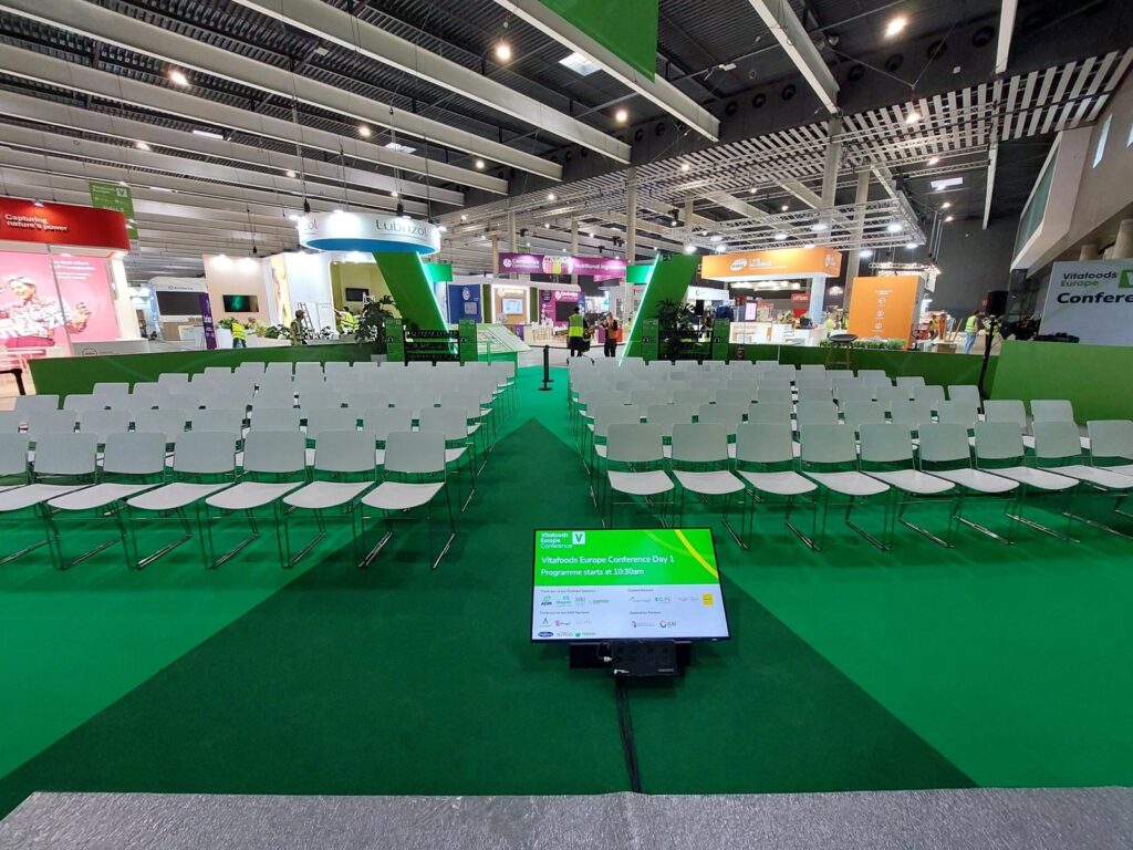 Rows of white conference chairs on green carpet at the Vitafoods Europe Conference during build-up
