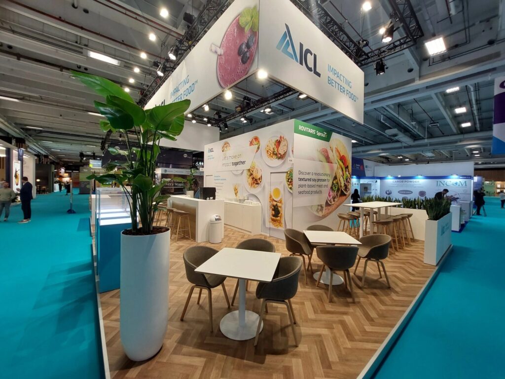 Café tables, grey bucket chairs and bar stools on the ICL stand at FI Europe 2025