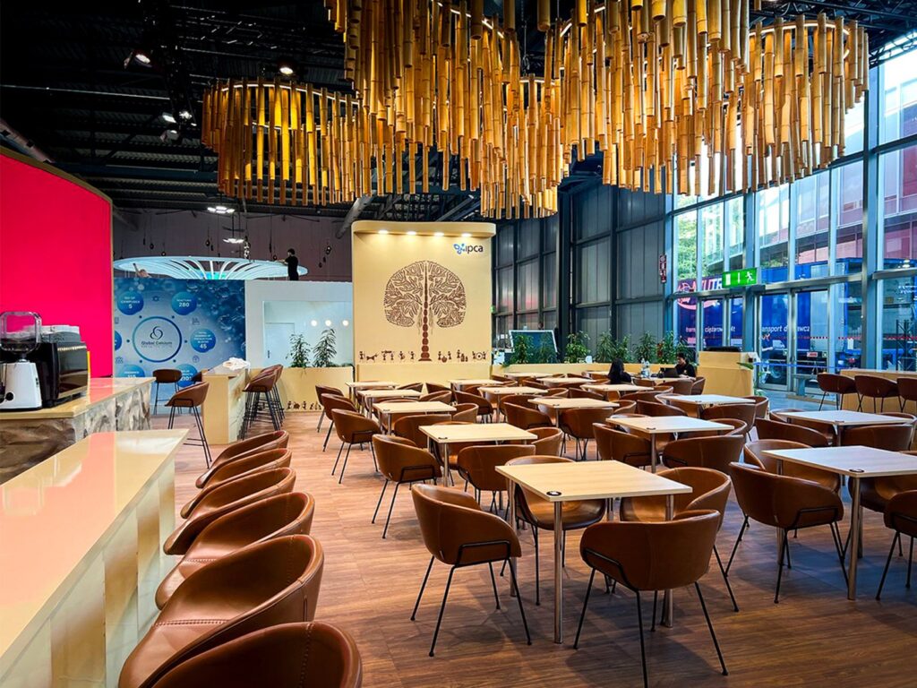 Hospitality area with tan leather chairs, wooden tables and bar stools on a stand at CPHI 2026