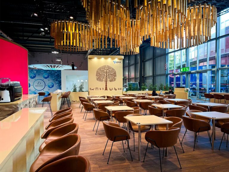 Hospitality area with tan leather chairs, wooden tables and bar stools on a stand at CPHI 2026