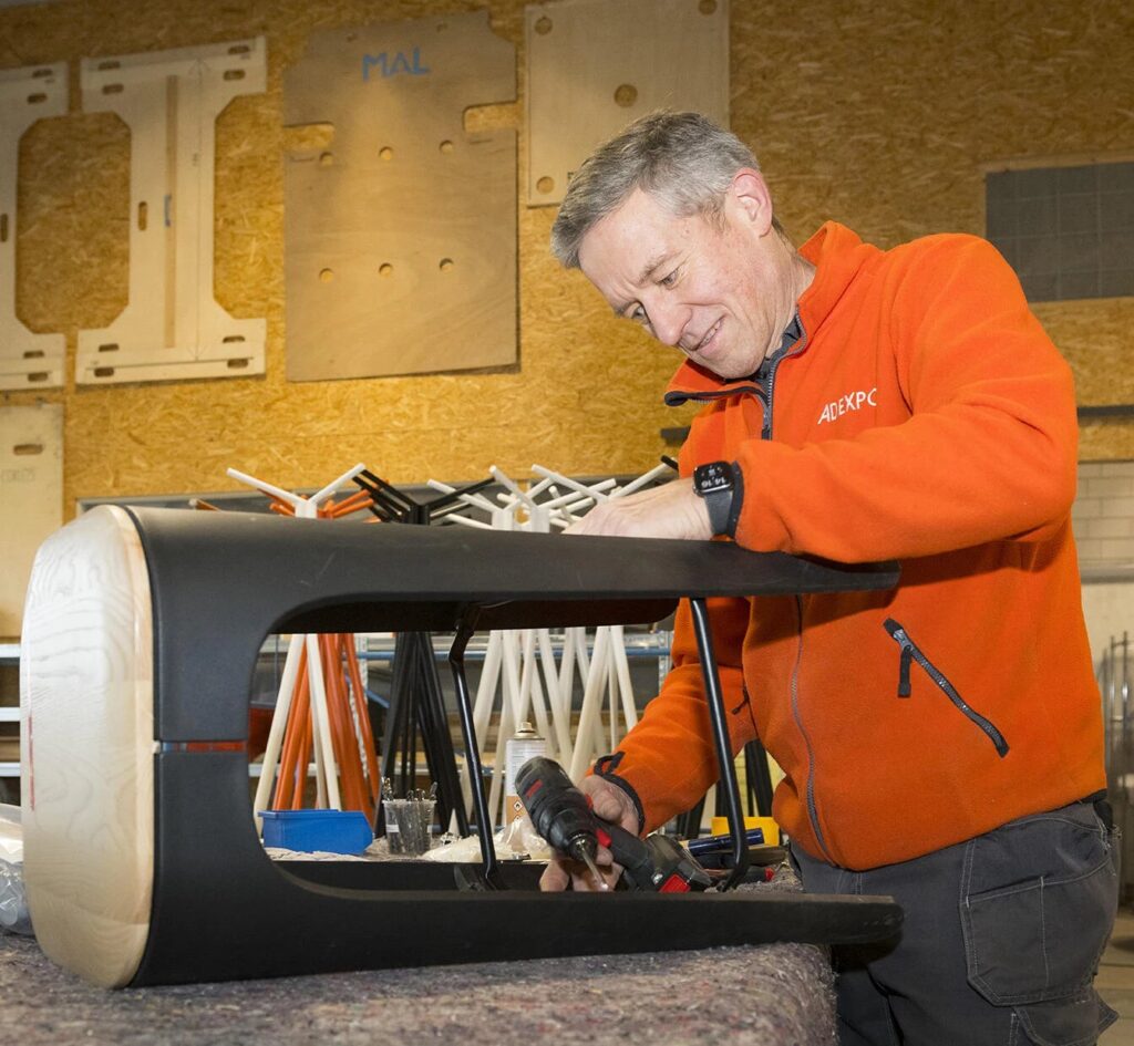 Adexpo staff member in branded fleece assembling a furniture piece in the warehouse workshop