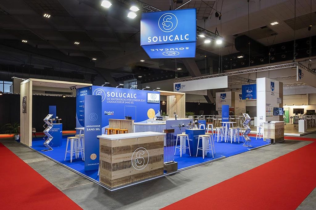 Solucalc stand at Batibouw with blue floor, hanging banner and reclaimed-wood counters