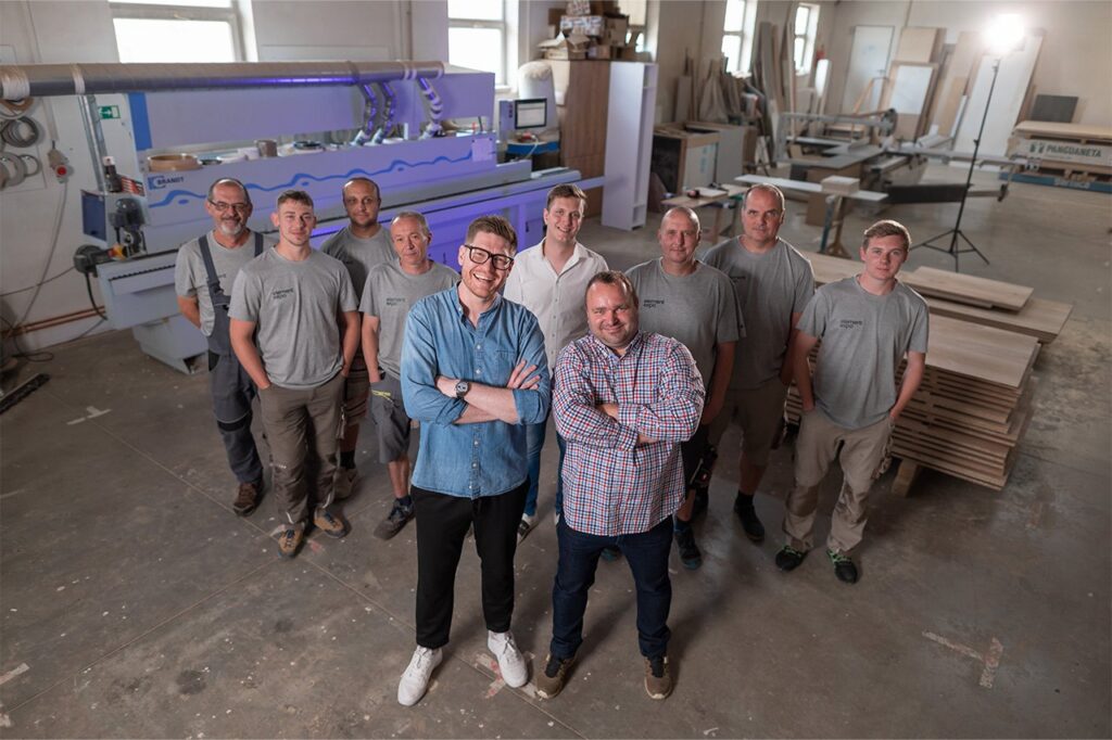 Element Expo team in branded grey T-shirts posing in their joinery workshop beside an edge-banding machine