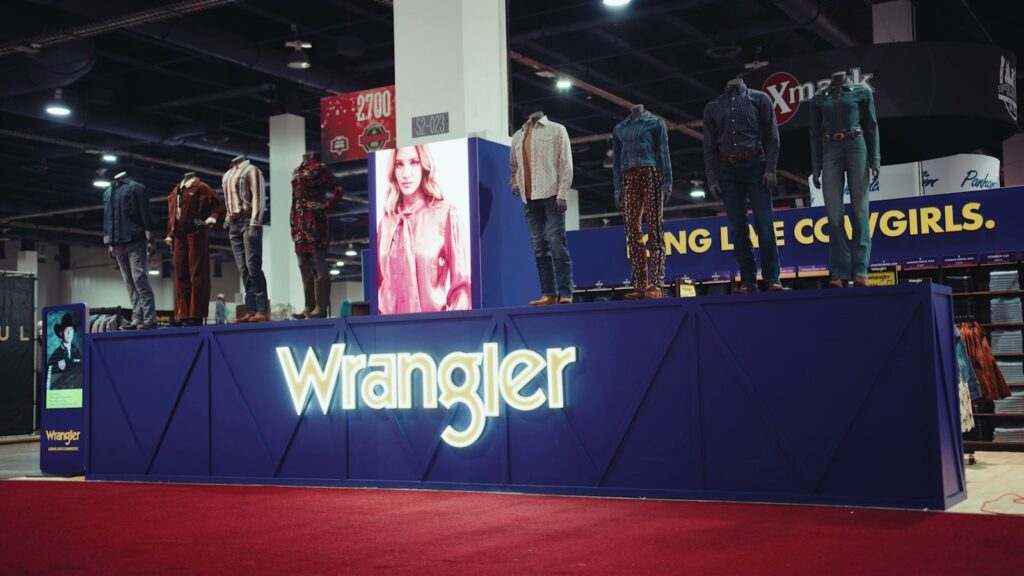 Wrangler exhibit with mannequins on a raised blue platform and backlit Wrangler sign on a show floor