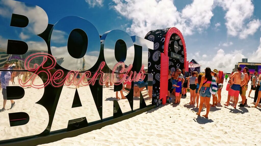 Boot Barn Beach Club mirrored letters and bandana-print arch with visitors on the sand