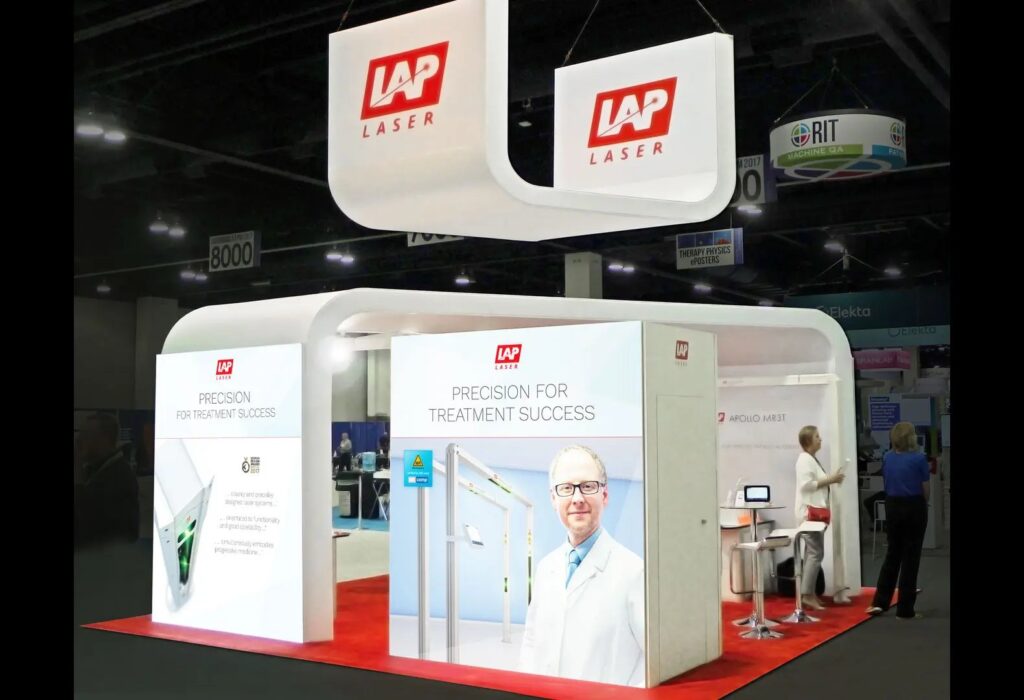 LAP Laser booth with curved white frame, hanging U-shaped sign, red flooring and staff talking with visitors