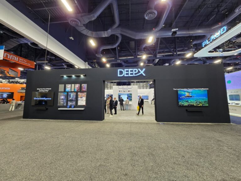 Black DEEPX stand front with backlit logo, two display screens and central entrance on a carpeted aisle