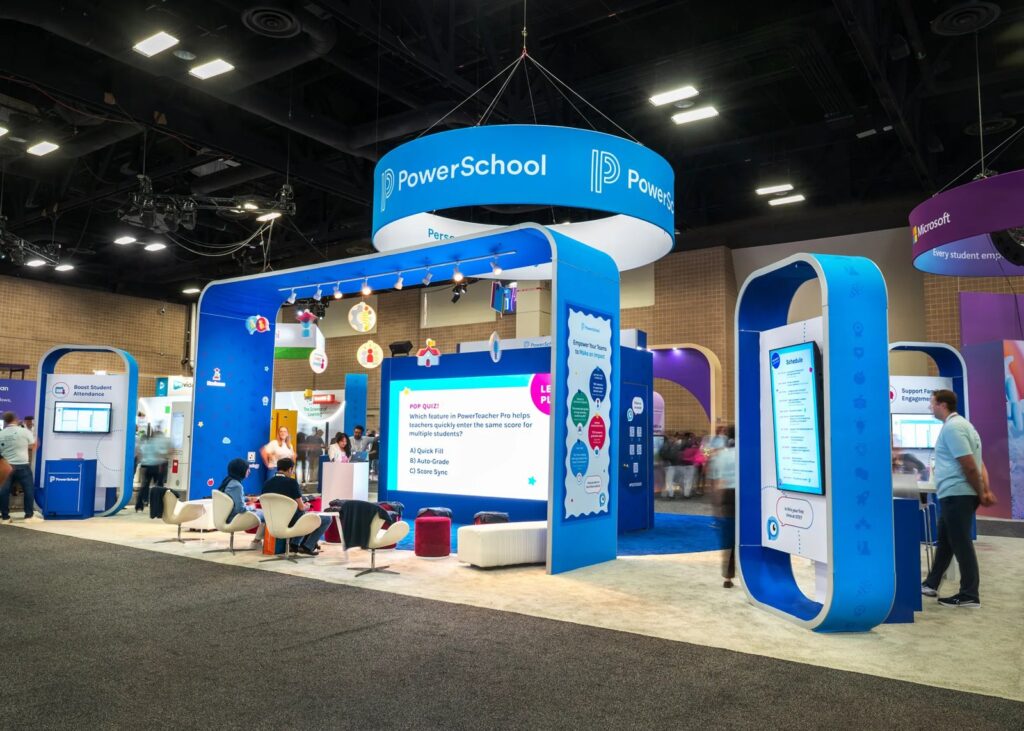 PowerSchool stand at ISTE with blue arches, hanging ring sign, lounge seating and screens