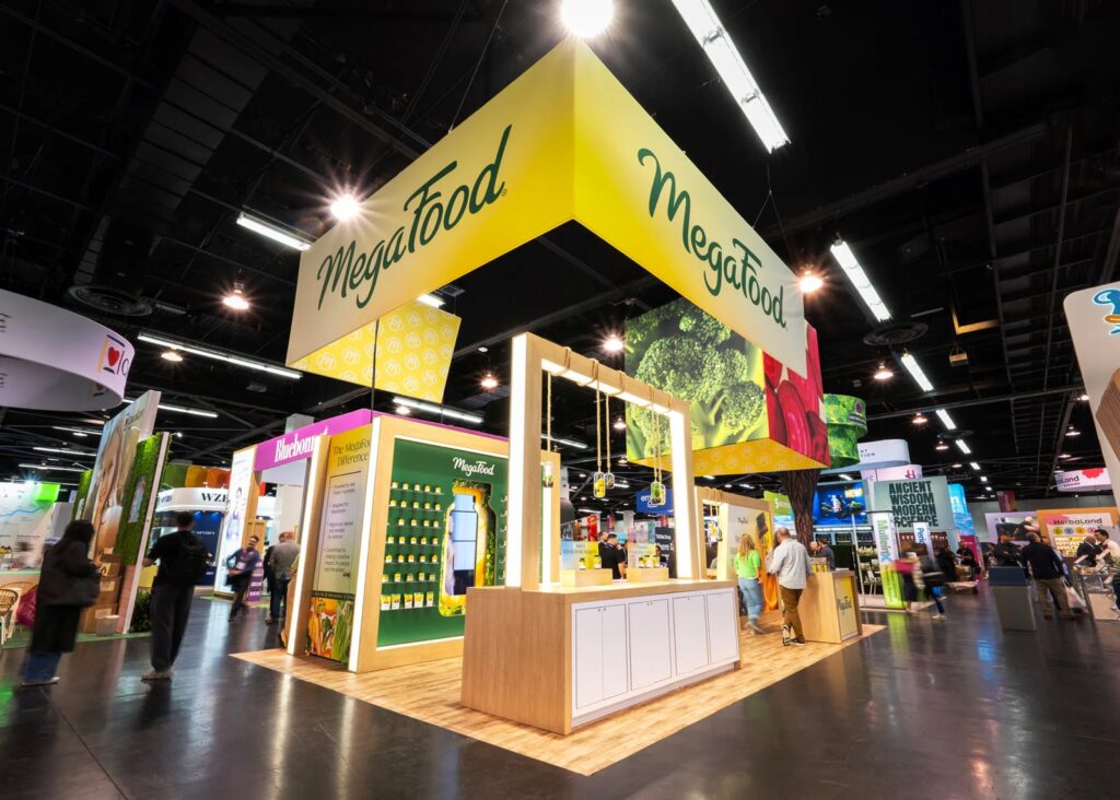 MegaFood island stand with a yellow hanging sign, wooden counters and product wall at Expo West