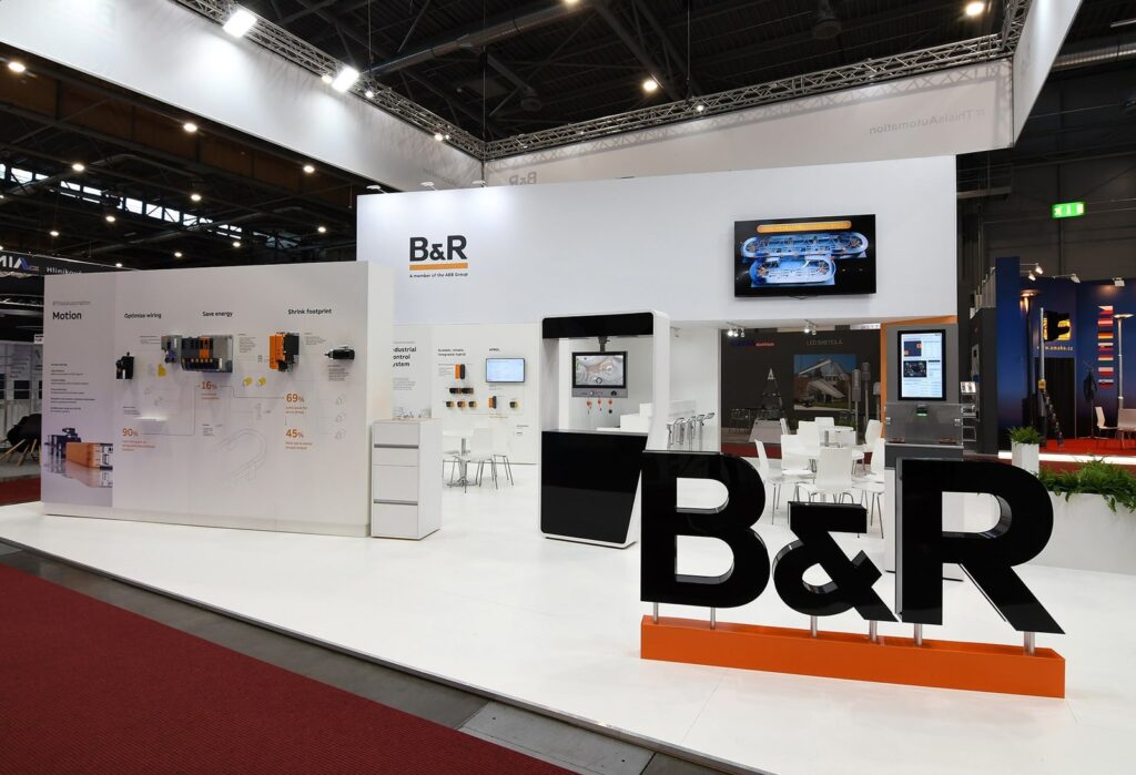 White B&R stand with large 3D letters, product wall graphics and a meeting area at Amper Brno