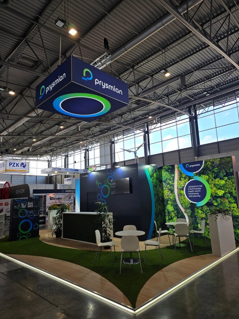 Prysmian stand with a hanging illuminated sign, artificial grass floor and forest wall graphic at Amper Brno
