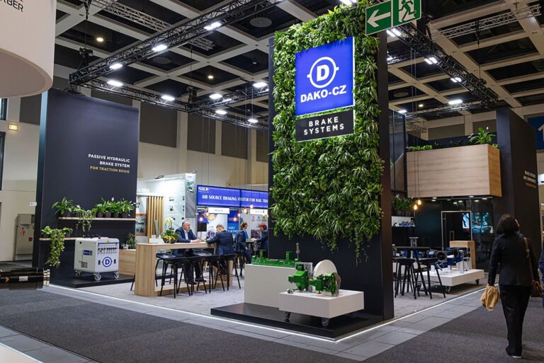 DAKO-CZ brake systems stand with a living plant wall, wooden bar and visitors talking at InnoTrans Berlin